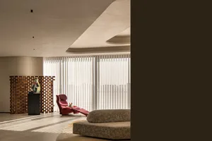 A modern minimalist living room with concrete walls and flooring, featuring a red lounge chair and a wooden sculpture.