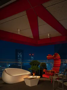 A modern outdoor seating area with a red chair and a white lounge chair, featuring a concrete flooring and a ceiling covered 