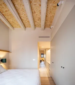 A minimalist bedroom with a white bed, wooden nightstand, and white curtains.