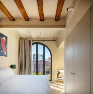 Modern minimalist bedroom with wooden beams on the ceiling, fabric curtains, and a white bed.