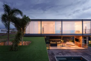 A modern house with glass walls and a backyard featuring green grass and a swimming pool.