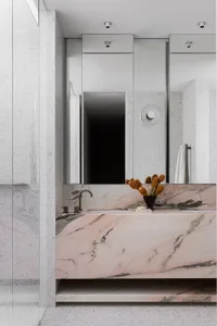 Modern bathroom with white and pink marble walls, a floating sink with a pink marble countertop, and a vase of pine cones on