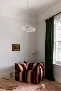 A modern living room with a striped cushioned chair, a glass side table, and a lamp with a unique design.