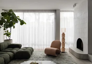 A modern living room with a green couch, beige chair, concrete fireplace surround, and frosted glass floor lamp on a plush ru