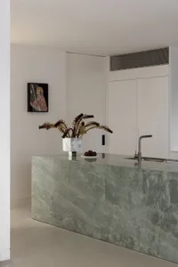 A modern kitchen with a marble countertop featuring a vase of flowers and a plate of fruit.