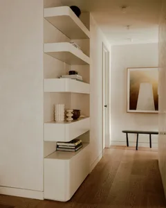 A modern minimalist living room with sleek, white shelves, wooden flooring, and a black bench with a framed abstract artwork.