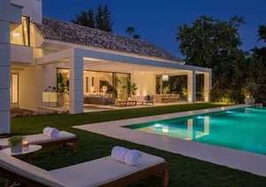 Modern residential exterior with a pool house, featuring concrete materials and warm lighting at dusk.