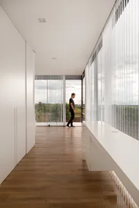 Man standing in a modern residential interior with large glass walls, showcasing a minimalist design with natural light.