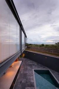 A modern residential terrace featuring a glass-walled swimming pool, surrounded by concrete and adorned with a tiled floor.