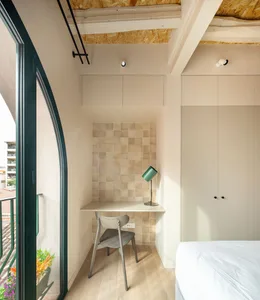 A minimalist bedroom featuring a white bed with a green lamp and a wooden floor.