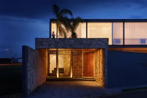 A modern house with a stone-clad exterior at night, illuminated with warm lighting.