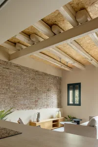 A modern living room with exposed brick walls and wooden beams on the ceiling.