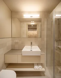 A minimalist bathroom with white tiles, a floating sink, and a glass-enclosed shower.