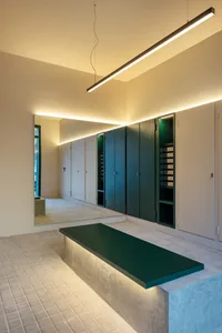 A minimalist interior space featuring a green bench with integrated lighting against a concrete wall with built-in storage ca