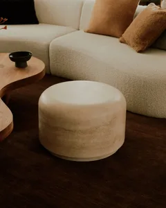 A modern living room with a white sectional sofa, brown throw pillows, a wooden curved coffee table, and a concrete cylindric