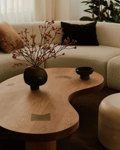 A modern living room featuring a wooden side table with a vase of flowers and a bowl on top, surrounded by a comfortable couc