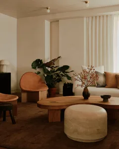 Modern minimalist living room featuring natural wood and concrete furniture, with potted plants, a round coffee table, and a 
