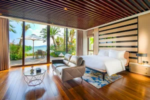 A modern bedroom featuring a large bed, leather sofa, and glass door with a water view.