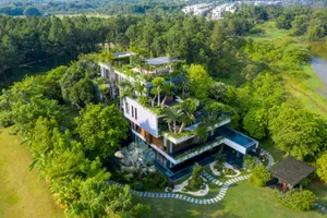 A modern house exterior surrounded by trees and greenery, featuring a metallic roof and outdoor seating areas.