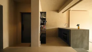 A minimalist residential kitchen with a concrete countertop island, black shelving unit, and a door in the background.