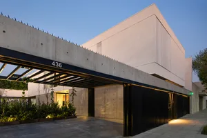 Modern, minimalist concrete building with drive-through garage and greenery in foreground.