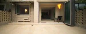 A modern residential entryway featuring a brick and concrete mix, with a large window, a bench, and a folded glass door leadi