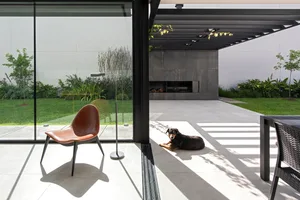A modern patio with concrete flooring and a brown leather chair, featuring a dog lying on the ground and a grill area.