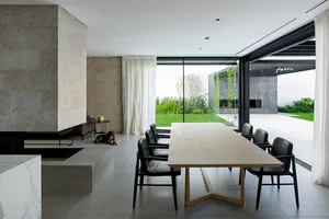 Contemporary residential dining room featuring a long wooden table, black chairs, concrete floors, and a large window overloo
