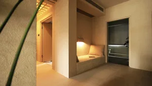 A minimalist interior space featuring a concrete seating area with a cushion and a soft-lit lamp on a beige wall, adjacent to