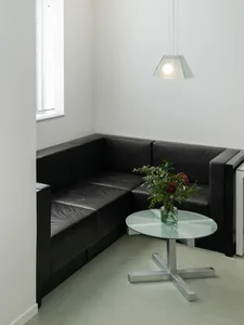 A minimalist living room featuring a black leather sofa, a round glass coffee table, and a hanging pendant light.