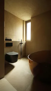 A modern bathroom with tiled walls and floor, featuring a sleek black toilet, a freestanding bowl-shaped bathtub with a metal