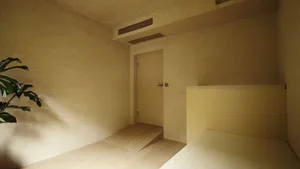 A minimalist bedroom featuring concrete walls and flooring, with a low bed and green plants.