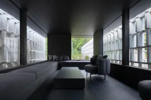 A minimalist room with concrete walls and large windows showing greenery outside.