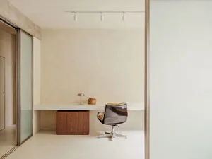 A minimalist office space featuring a concrete desk and chair, illuminated by track lighting.