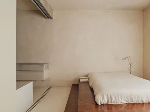A minimalist bedroom featuring a concrete bed platform on a wooden floor.
