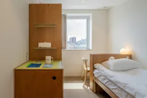 A minimalist bedroom featuring wooden furniture and a window with a view of a cityscape.