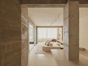 Minimalist living room with concrete walls, white couch, and leather chair.