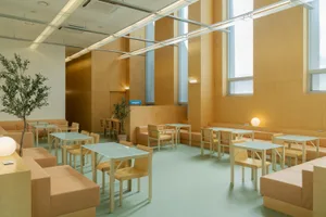 A cafe with modern wooden furniture, featuring tables and chairs arranged in a spacious, minimalist environment.