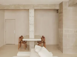 Modern dining room with minimalist design, featuring a concrete table and chairs arranged around it.