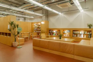 Modern library reading room with wooden furniture and shelves filled with books.