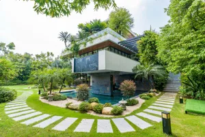 A contemporary residential house with glass walls and stone accents surrounded by lush greenery.