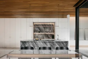 Modern kitchen featuring a marble countertop and island with black chairs and white cabinets.