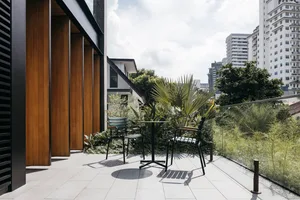 Concrete patio with modern black metal chairs and table, surrounded by greenery and topped with tropical plants.