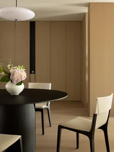 Minimalist dining room with a round wooden table, white chairs, and a white vase with flowers.
