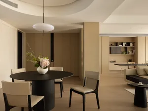 Modern living room with wooden board floor, beige furniture, and a black dining table with a vase of flowers.