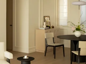 Modern living room with wooden flooring and furniture, featuring sleek white chairs and a round black table.