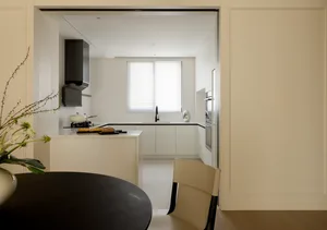 A modern kitchen with white cabinets, a black table, and a vase of flowers on the table.
