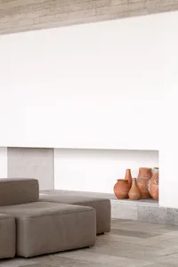 A modern living room with grey leather furniture and terracotta vases arranged on a white shelf.