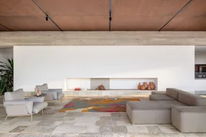 Modern living room with a concrete floor, gray lounge furniture, and a colorful rug in the center.