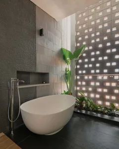 Modern minimalist bathroom featuring concrete and glass materials, with a freestanding bathtub, green plants, and a wall with